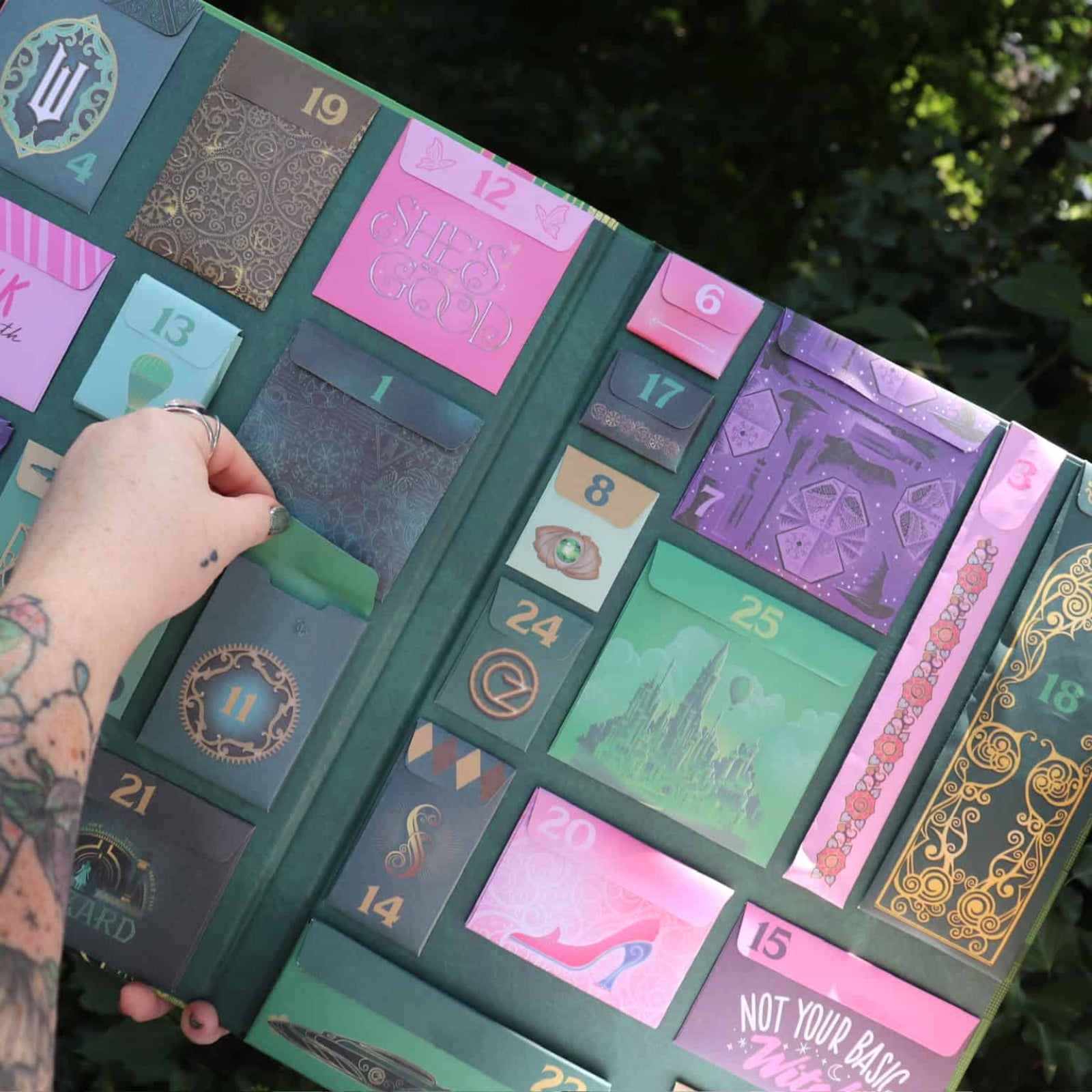 Advent calendar with variously colored panels, some with text and graphics, held by a person with tattoos.