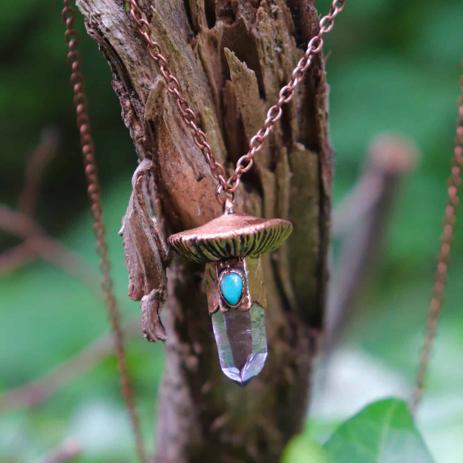 Close-up of mushroom necklace pendant with crystal and turquoise on tree bark