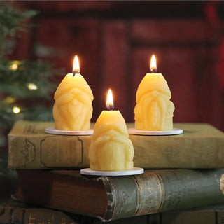 The Beeswax Holiday Gnomes on a stack of books in front of a Christmas tress.