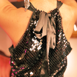 A woman wearing the Black Sequin Round Neck Mesh Tie Back Tank Top and showing off the tied back.