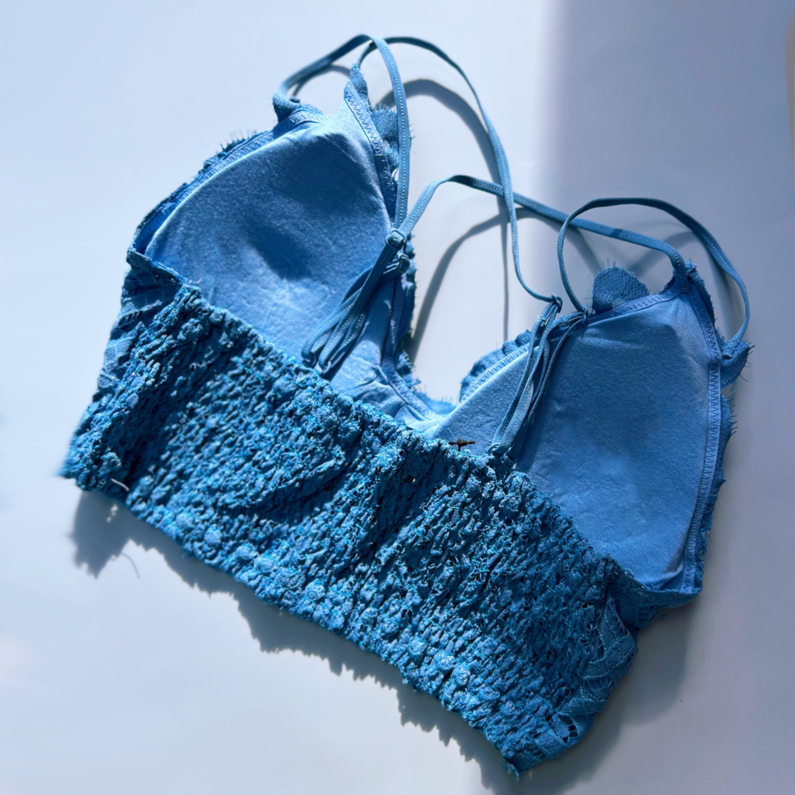 The blue Criss-Cross Back Lace Bralette on a blue background, showing off the back.