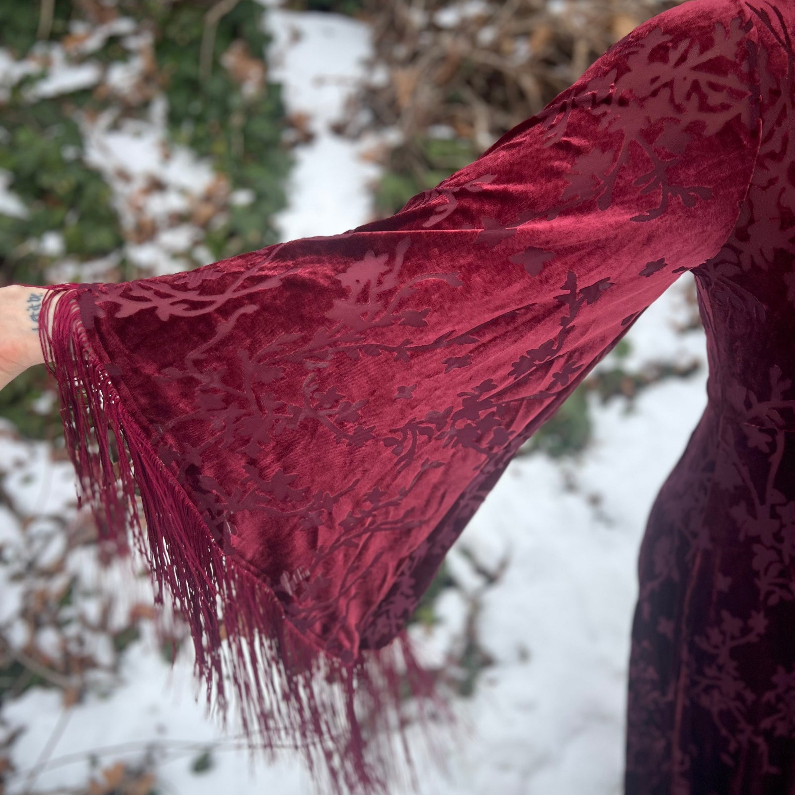 Close-up of a person wearing a burgundy dress with lace sleeves against a snowy background.