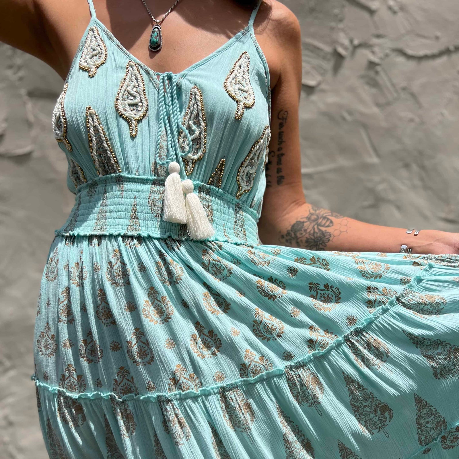 Mint green dress with intricate patterns and tassels against a stone wall background