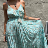Woman wearing a light blue floral bohemian dress against a stone wall.