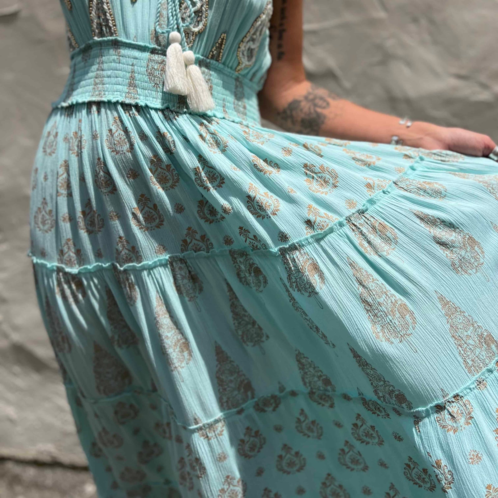 Light blue dress with intricate patterns and tassel details against a neutral background
