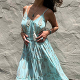 Woman in a light blue dress with floral patterns against a textured stone wall.