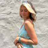 Woman in a light blue dress with floral patterns against a textured gray wall.