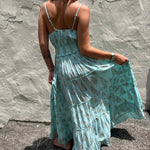 Woman wearing a light blue floral maxi dress against a textured stone wall.