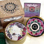 The Libra Crystal Candle opened with the lid to the right of it. The packaging of the Libra Crystal Candle is behind the candle next to a card.