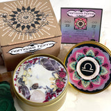 The Libra Crystal Candle opened with the lid to the right of it. The packaging of the Libra Crystal Candle is behind the candle next to a card.