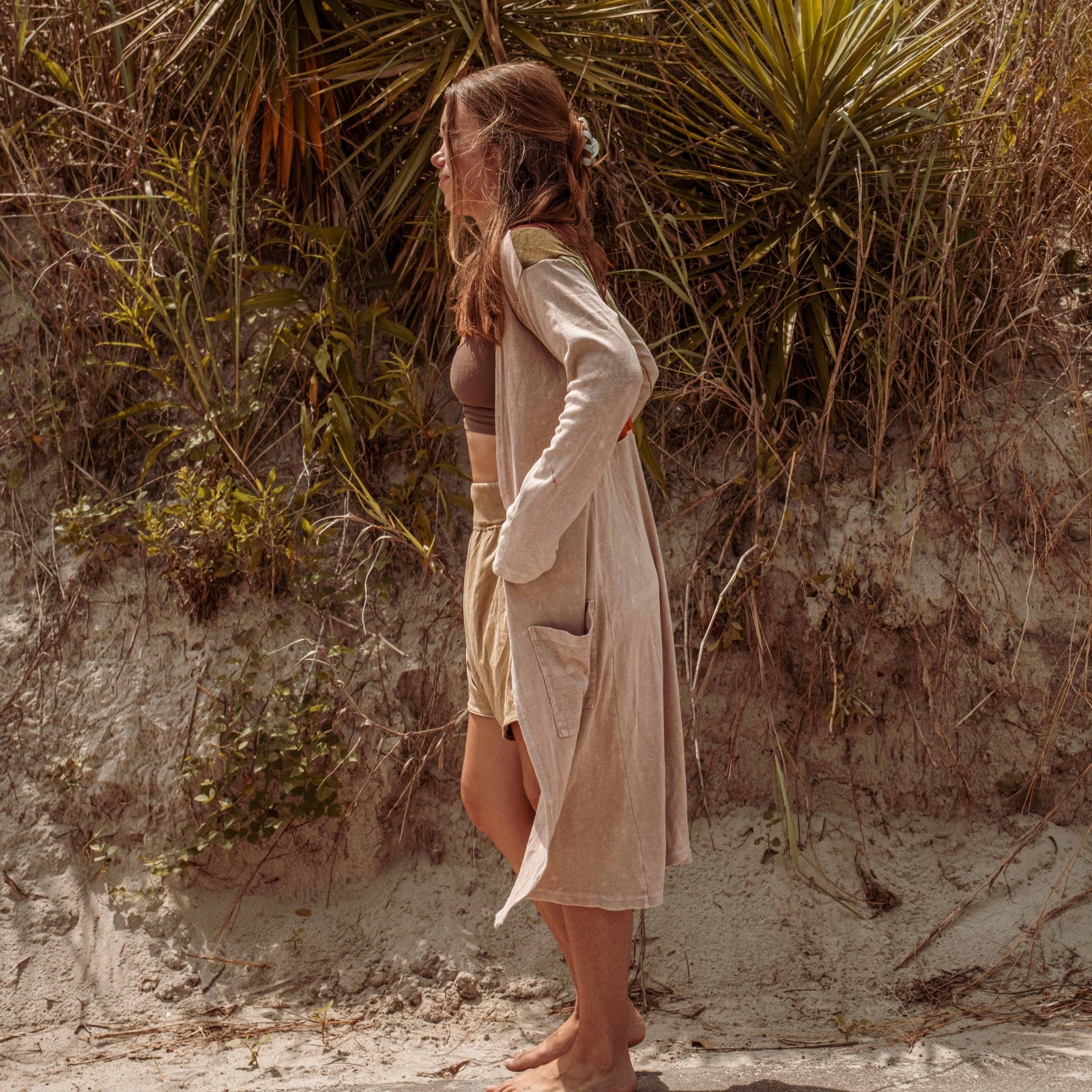 A woman wearing the earthy Sun Ray Cardigan in front of a sand dune at the beach.