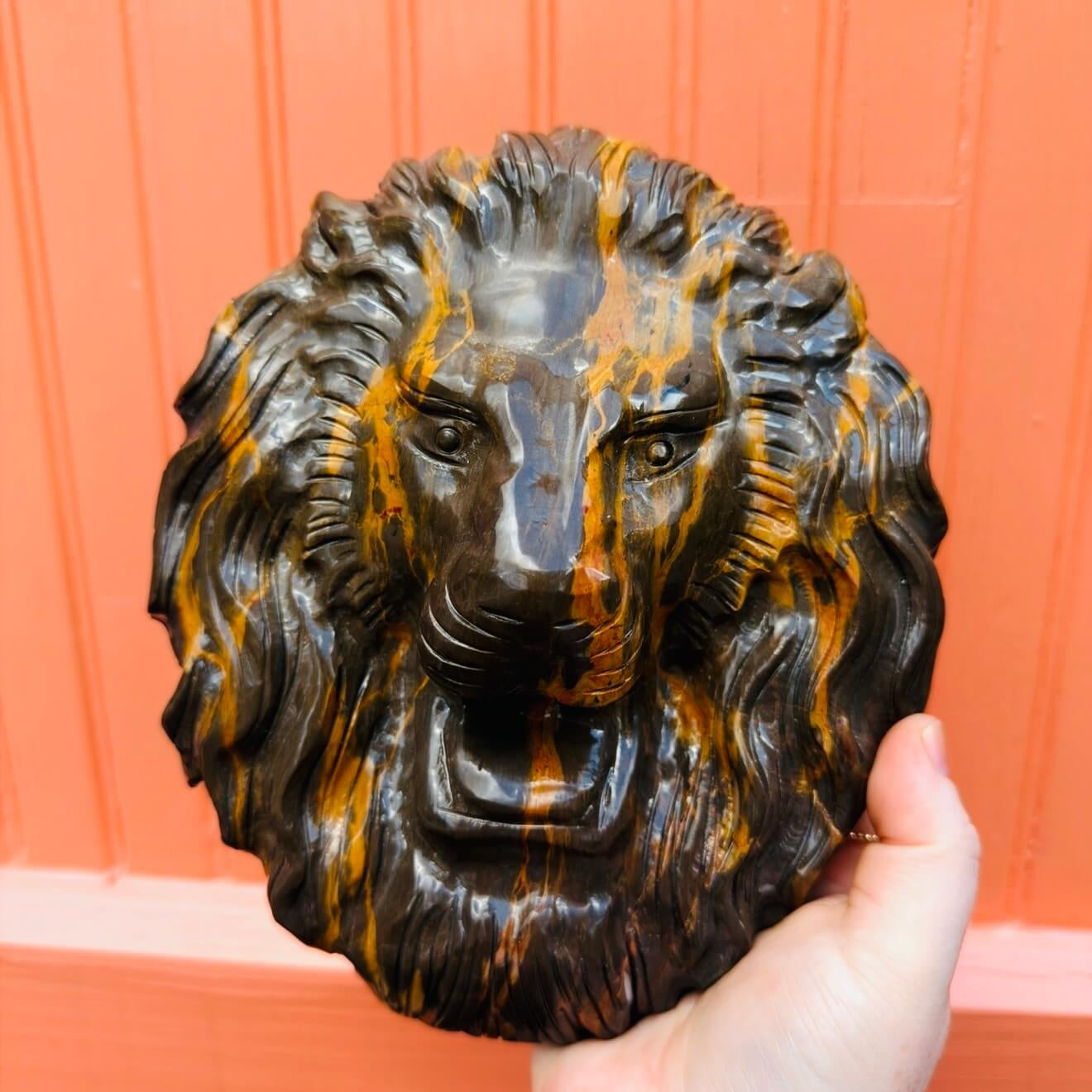 Close-up of a polished chocolate opal lion head crystal carving showing its detailed mane and golden orange veining