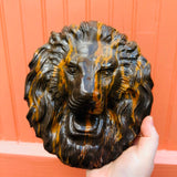 Close-up of a polished chocolate opal lion head crystal carving showing its detailed mane and golden orange veining