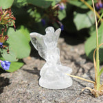 Crystal clear quartz fairy figurine on a natural stone surface with greenery in the background