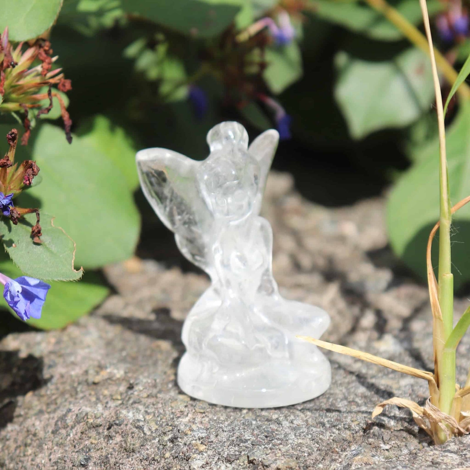 Crystal clear quartz fairy figurine on a natural stone surface with greenery in the background
