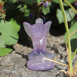 Purple fairy figurine on a natural background with green leaves and plants.