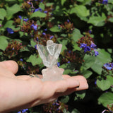 Crystal angel figurine held in a hand with a natural background of green leaves and purple flowers