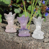 Three fairy figurines made of different colored crystals on a natural stone surface with greenery in the background.