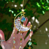 Someone holding the Opalite Crystal Moon Sun catcher with greenery in the background.