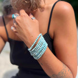 Person wearing multiple turquoise beaded bracelets on a blurred background