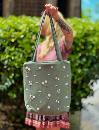 Blonde woman wearing a floral dress and carrying a sage green linen tote bag with hand-embroidered white daisies