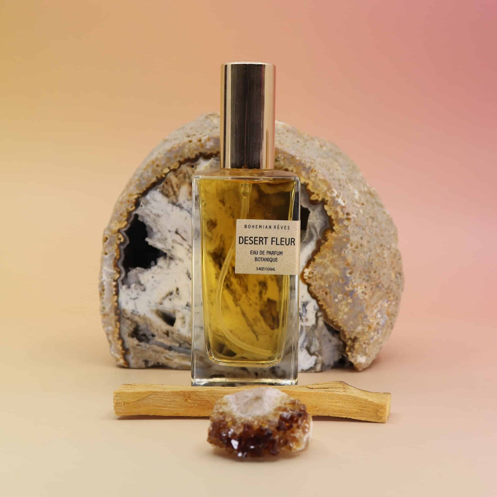 Perfume bottle labeled 'Desert Fleur' with a rock and wooden stick on a gradient background