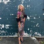 Woman in a colorful disco dress standing against a peeling blue wall.