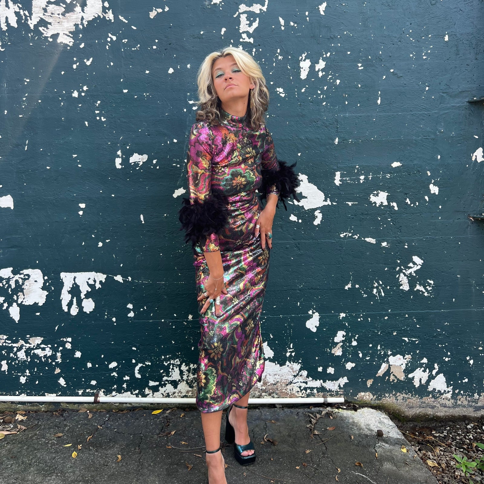 Woman in a colorful disco dress standing against a peeling blue wall.