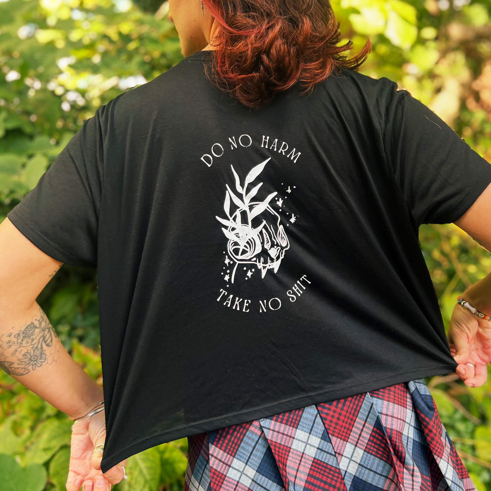 A woman wearing the Do No Harm Take No Sh*t Cropped Top with a red and navy plaid skirt, showing off the back.