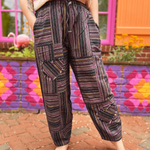 Person wearing patterned pants standing in front of a colorful mural.