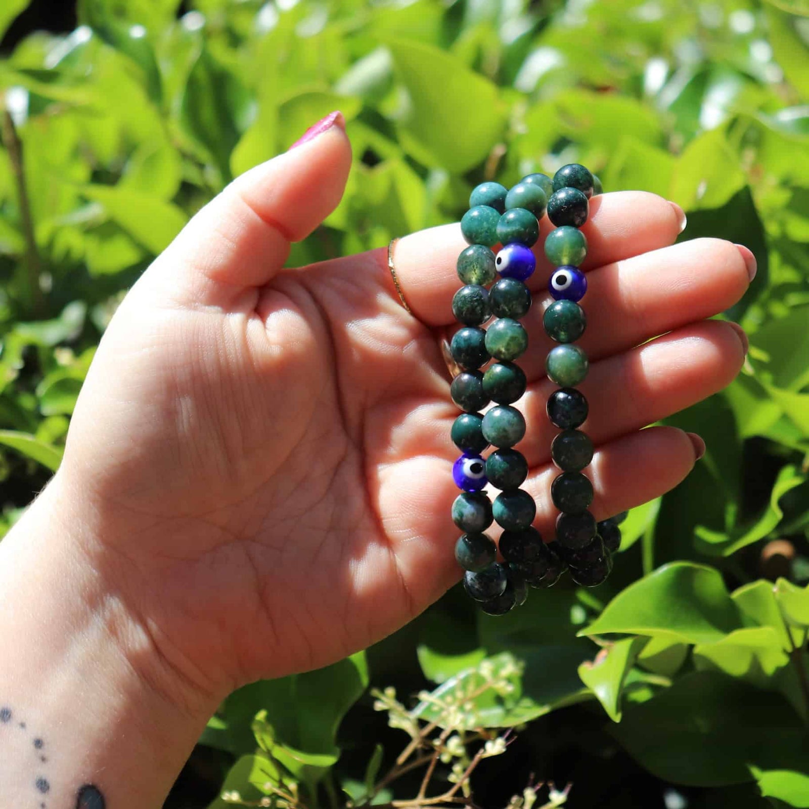 Hand holding Moss Agate evil eye bracelet outdoors
