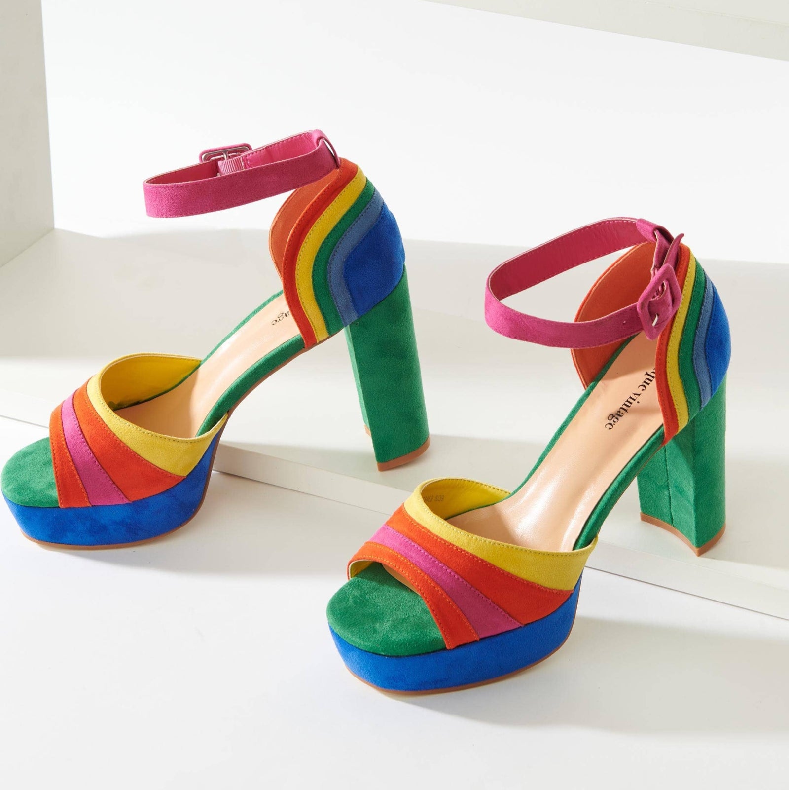 A pair of multicolored rainbow suede peep toe pumps with ankle straps and a chunky heel.