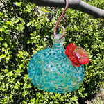 Handmade colorful glass hummingbird feeder hanging from tree branch outdoors