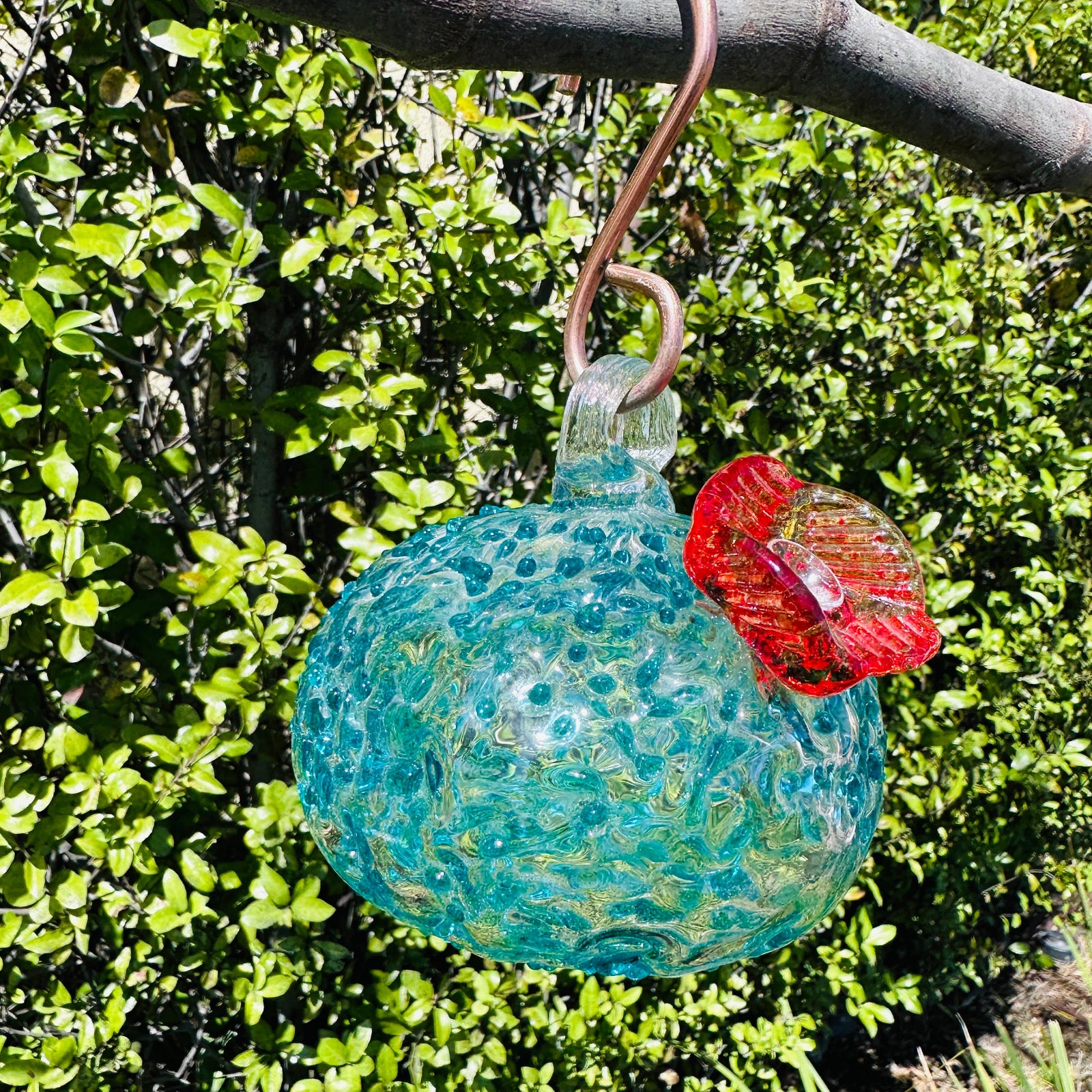 Handmade colorful glass hummingbird feeder hanging from tree branch outdoors