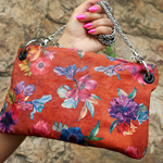 Someone holding the Orange Floral Print Italian Leather Crossbody Bag in front of a stone background.