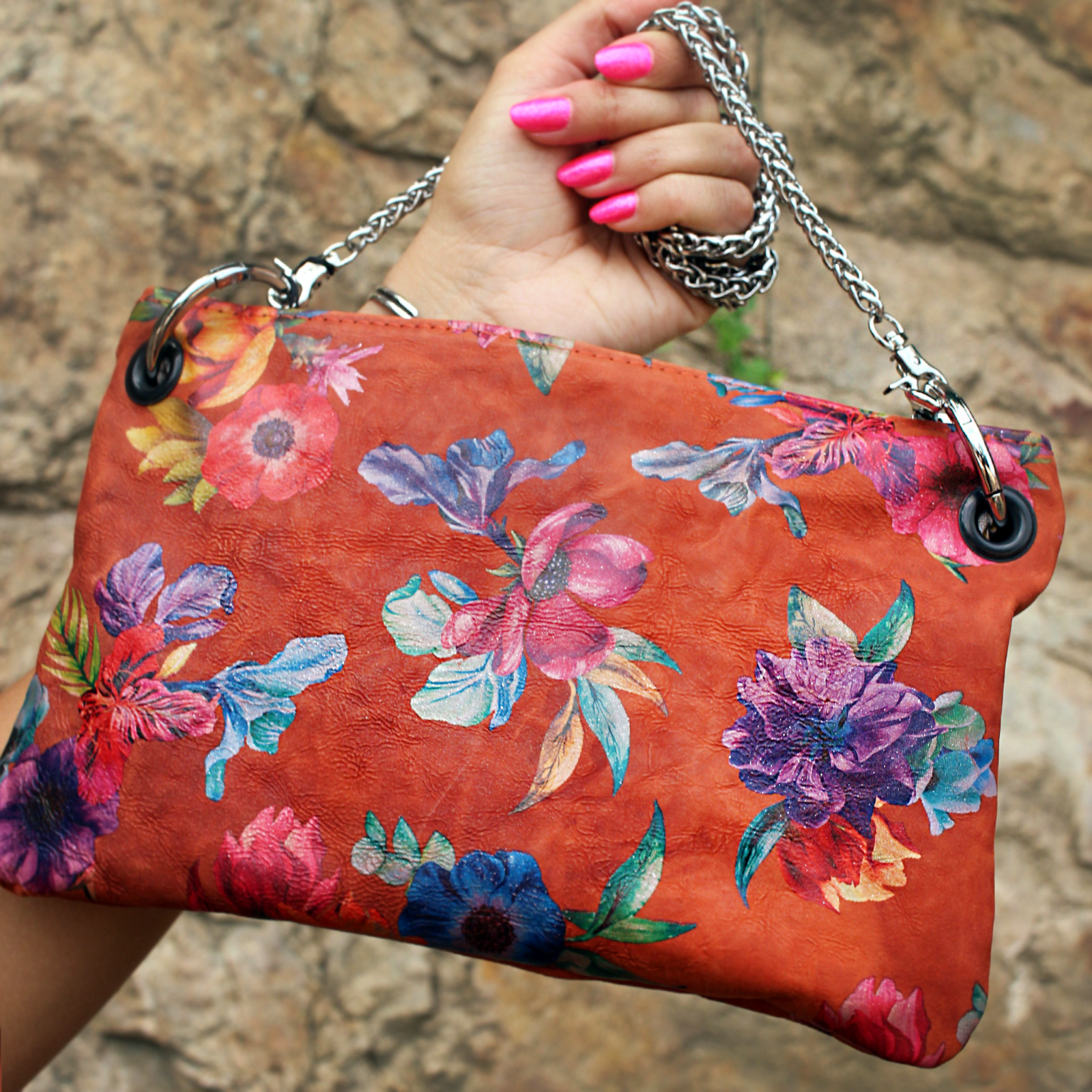 Someone holding the Orange Floral Print Italian Leather Crossbody Bag in front of a stone background.