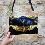 Someone holding the Small Black and Gold Heron Velvet Crossbody Bag in front of stone background.