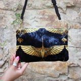 Someone holding the Small Black and Gold Heron Velvet Crossbody Bag in front of stone background.