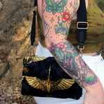 Someone wearing the Small Black and Gold Heron Velvet Crossbody Bag with a white skirt and a tie dye tank.