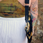 Someone wearing the Small Black and Gold Heron Velvet Crossbody Bag with a white skirt and a tie dye tank.