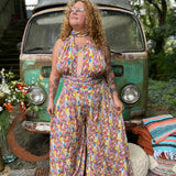 Woman in a colorful jumpsuit standing in front of a vintage van with nature in the background