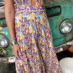 Person wearing a colorful patterned jumpsuit standing next to a vintage green truck.