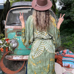 Person wearing a green patterned kimono and brown hat in front of a vintage van.