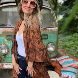 Woman in a patterned jacket and hat standing in front of a vintage van with a colorful blanket.