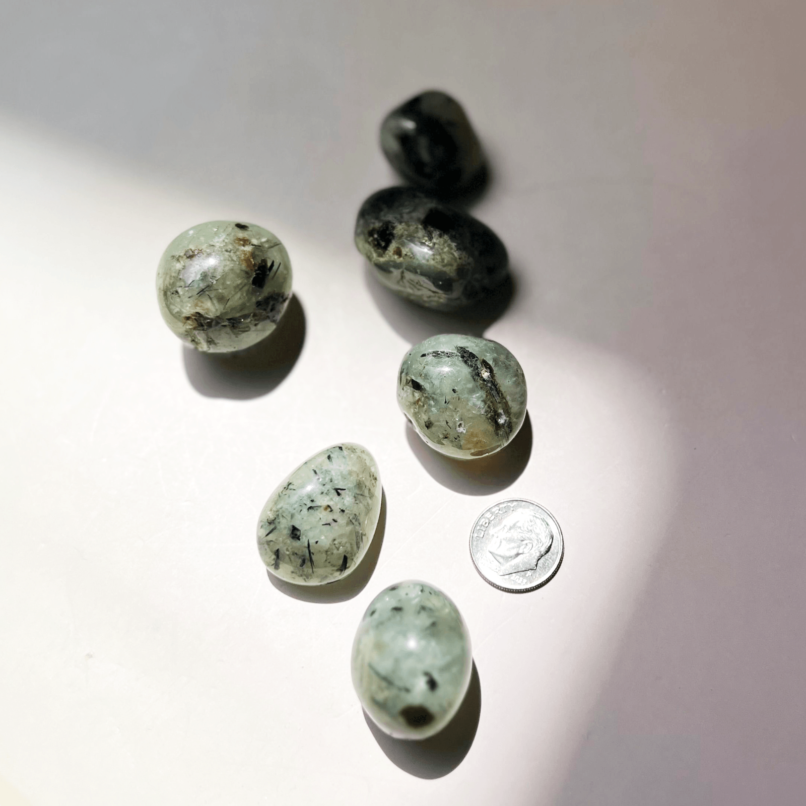 Prehnite crystal tumbles with coin for size showing natural green color and inclusions