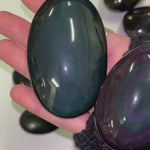 hand holding 2 rainbow obsidian palmstones showcasing the light