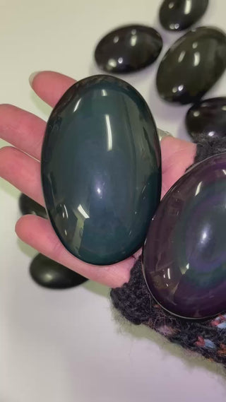 hand holding 2 rainbow obsidian palmstones showcasing the light