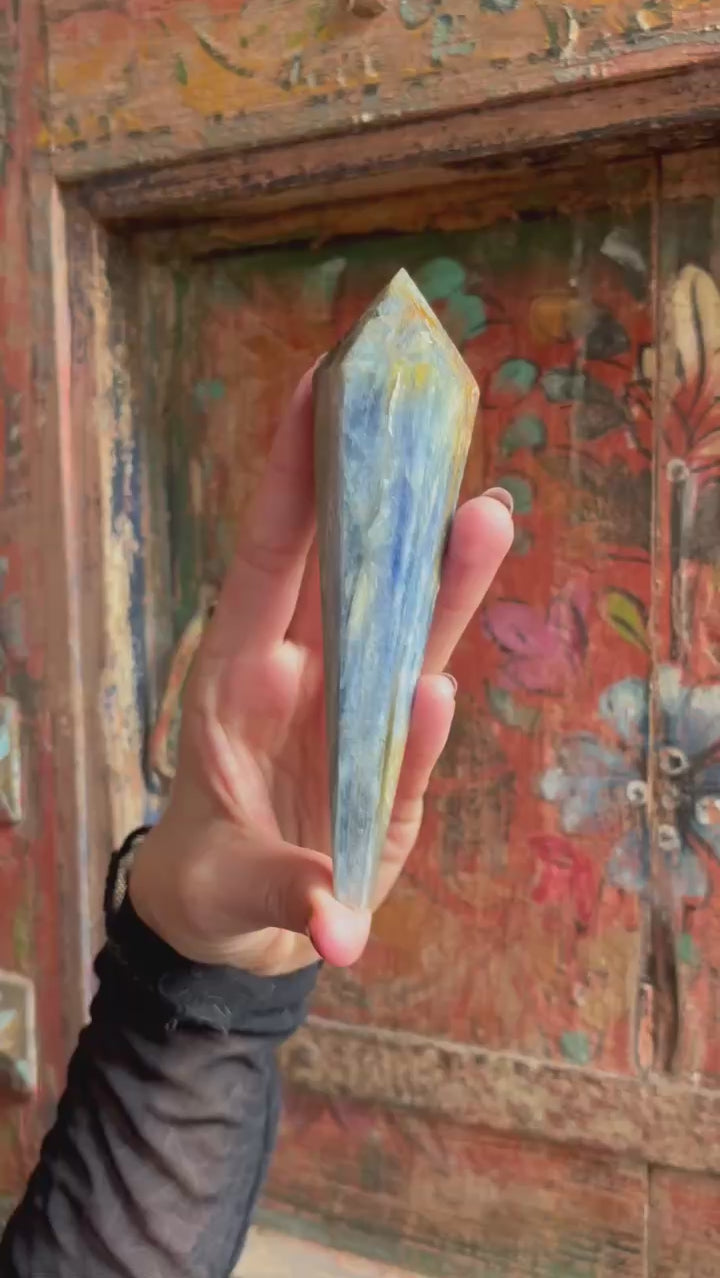 Blue Kyanite Crystal Scepter in hand in front of colorful door