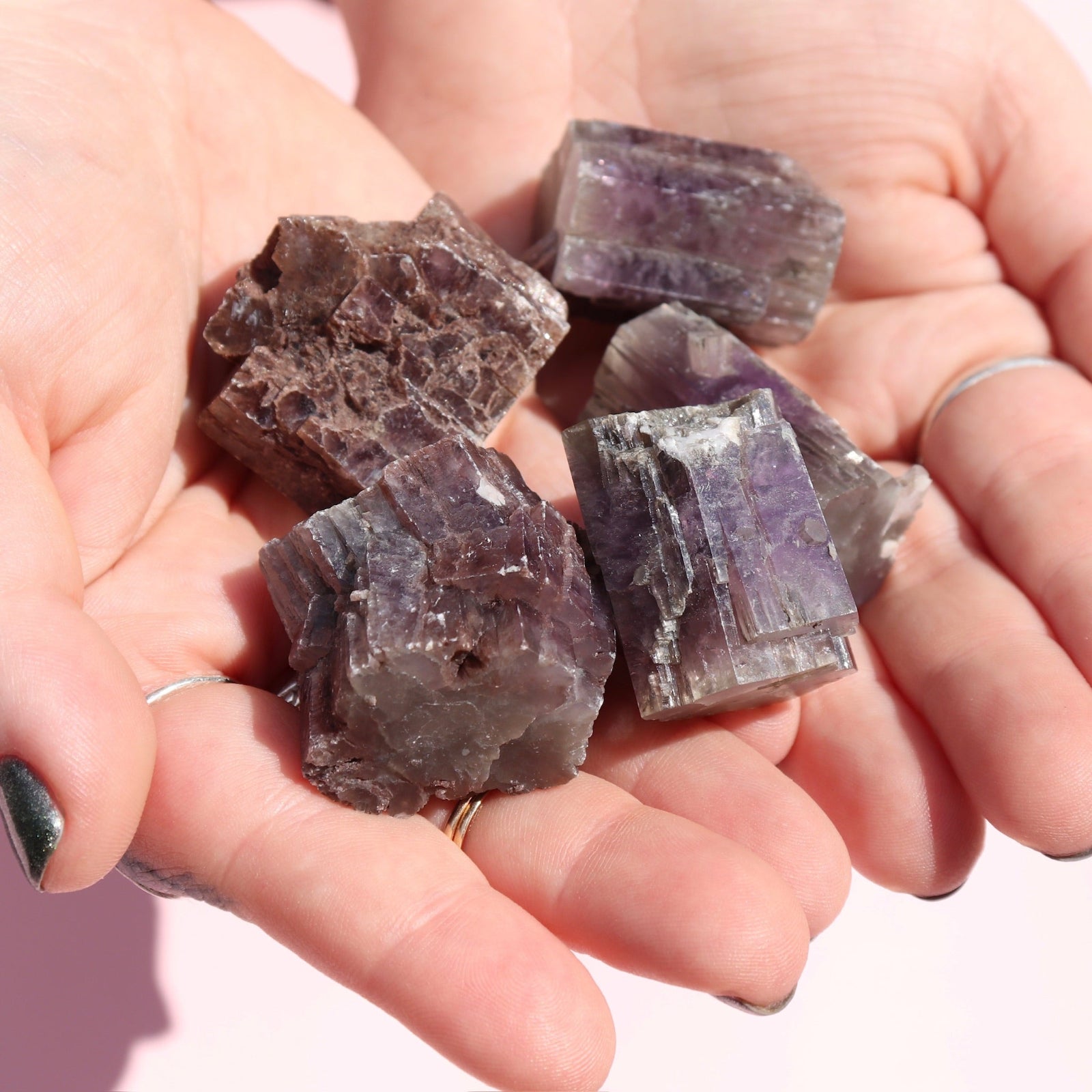 Hand holding purple crystal rocks against a neutral background