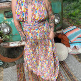Person wearing a colorful patterned jumpsuit in front of a vintage vehicle with a relaxed outdoor setting.